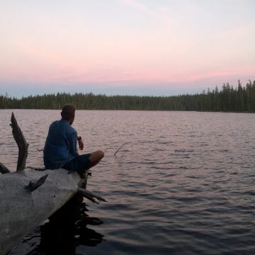 Mountain Man gazing out over Charlton lake at sunset from a dead log extending into the water