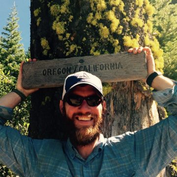Mountain Man posing with the Oregon California border sign