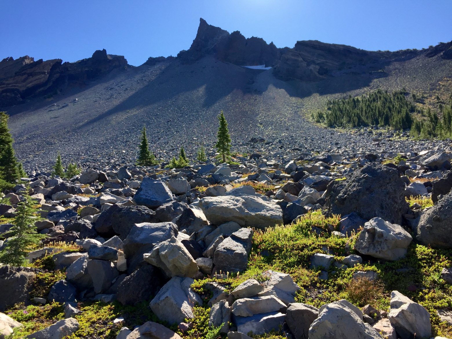 Sunlight over fields of rock leading up to the pointy summit of Mt. Thielsen