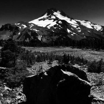 Looking back over a trailside boulder at a snow capped Mount Jefferson