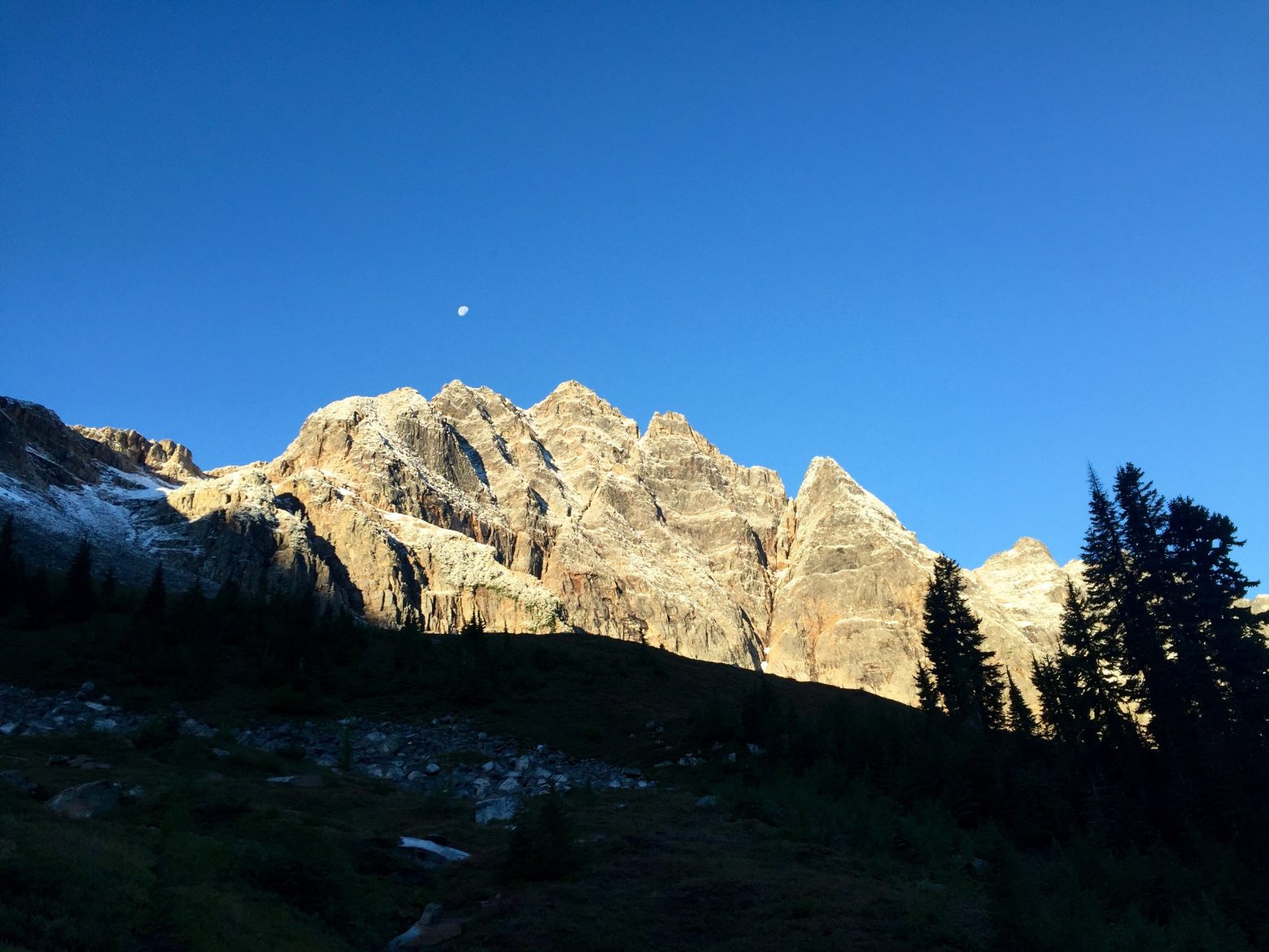 Blue sky behind jagged peak lit by the morning sun