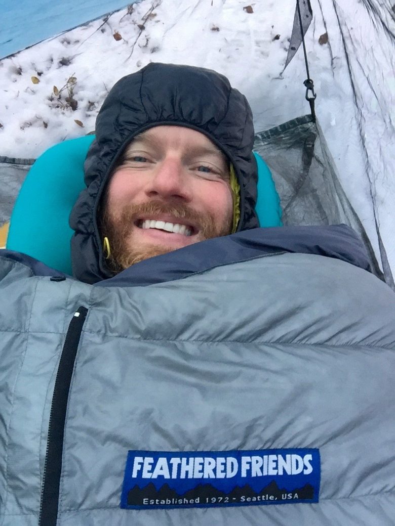 Mountain Man bundled up in sleeping bag on a cold snowy night