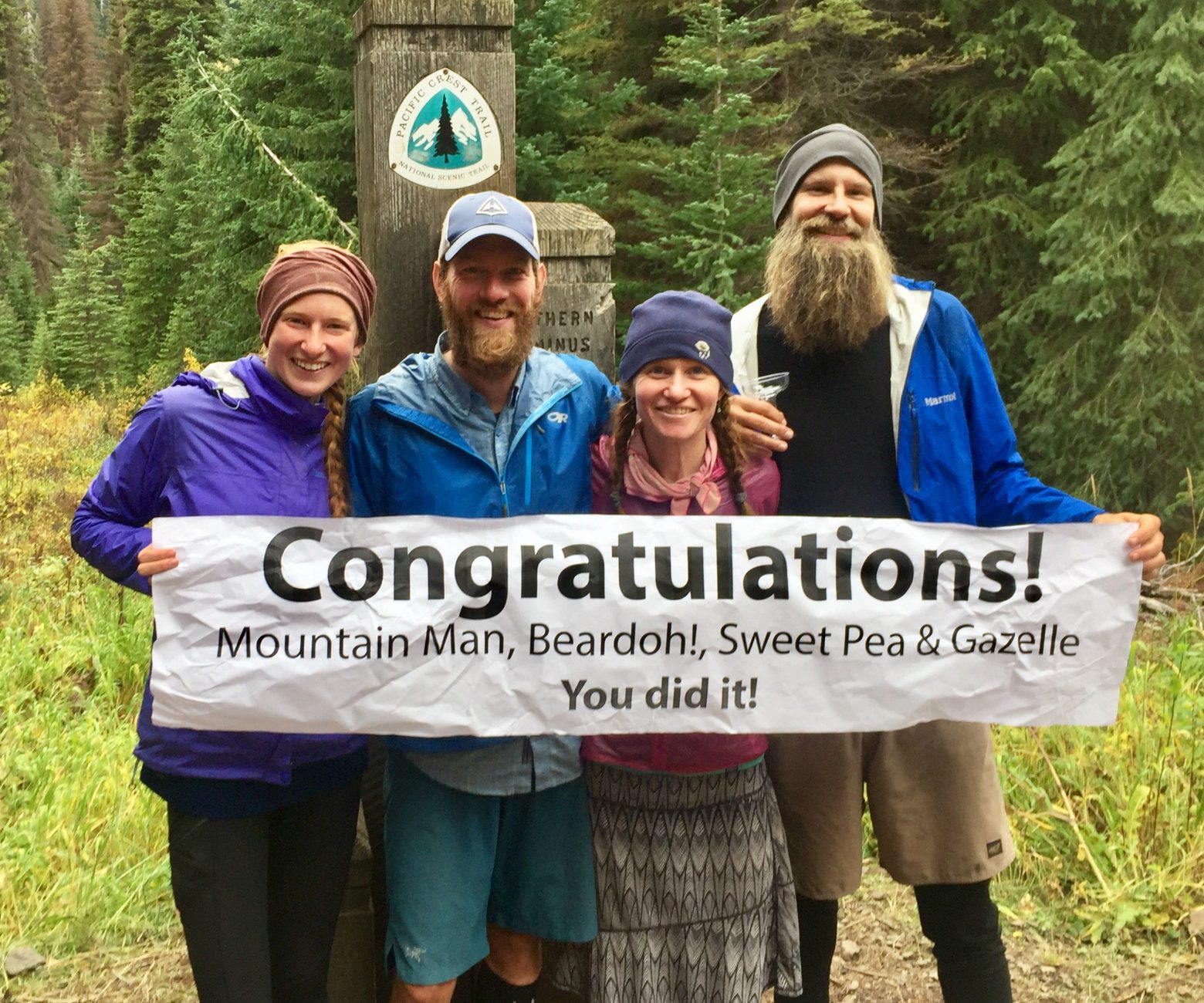 Mountain Man, Gazelle, Beardoh and Sweet Pea holding a congratulations banner at the PCT Northern Terminus